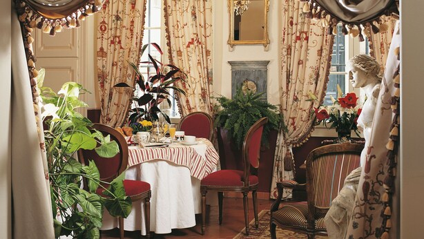A dining room with a table set for four, surrounded by chairs, a large mirror, and a statue. - Hôtel Cardinal (Aix-en-Provence)