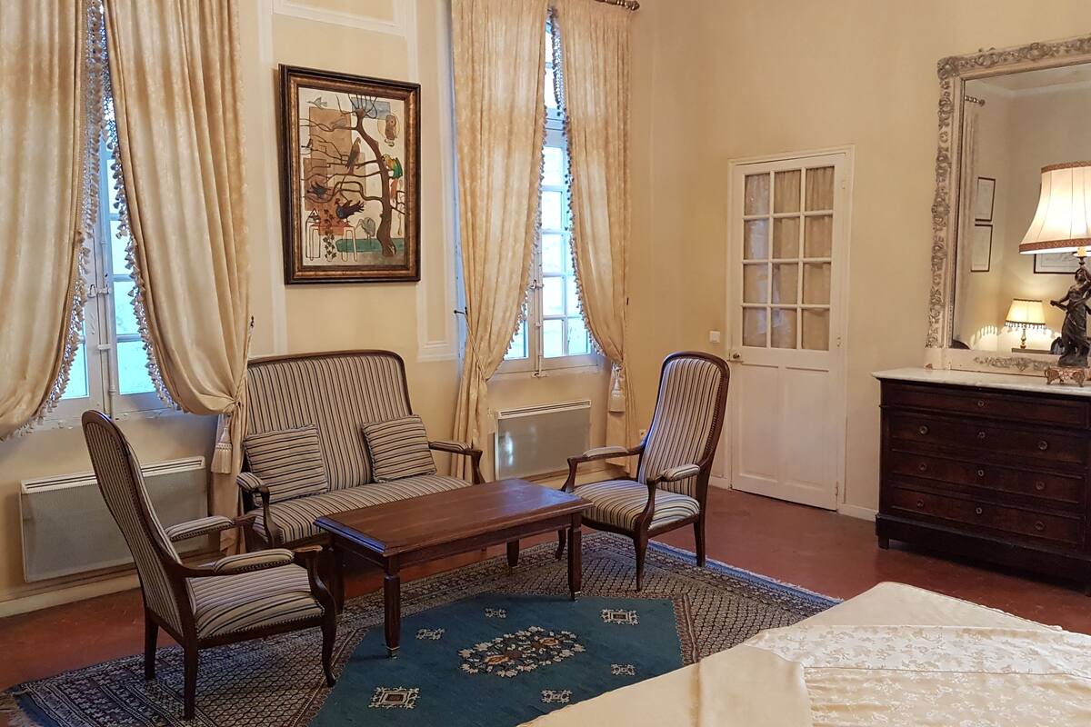 A hotel room with a striped sofa set, a wooden table, a dresser with a mirror, and a patterned rug.