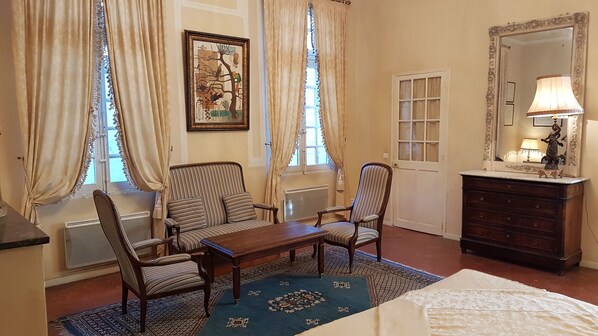 A hotel room with a striped sofa set, a wooden table, a dresser with a mirror, and a patterned rug. - Hôtel Cardinal (Aix-en-Provence)