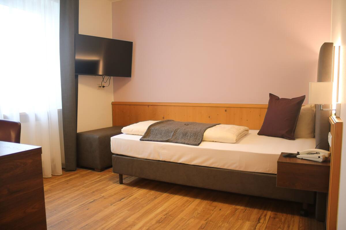 Een hotelkamer met een bed, nachtkastje, lamp en een aan de muur bevestigde televisie.