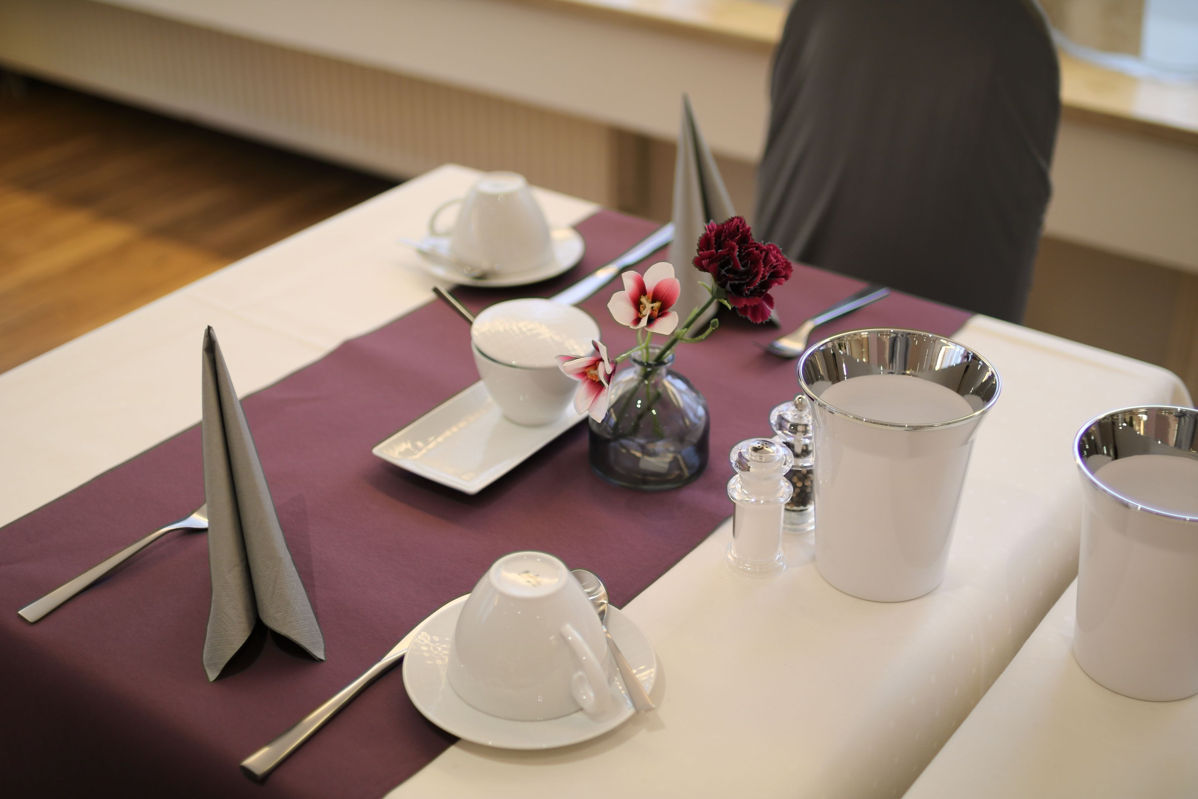 Ein Tisch gedeckt mit weißen Teetassen, Untertassen, einer Vase mit Blumen und einer Metallkanne.