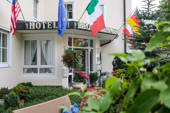 Ingresso di un hotel con bandiere, un cesto di fiori e piante in vaso.
