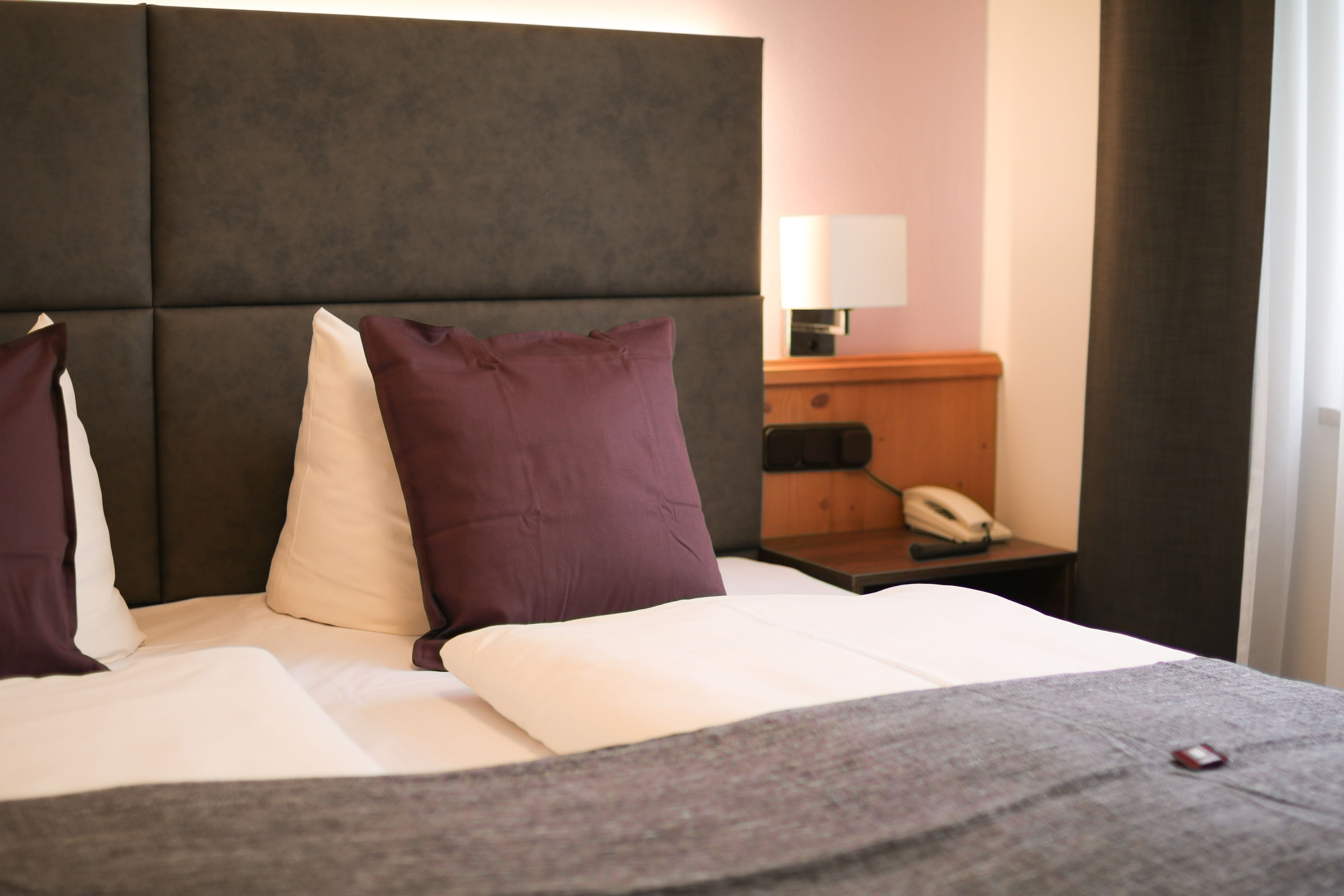A neatly made bed with a headboard, a bedside table with a lamp, and a telephone.
