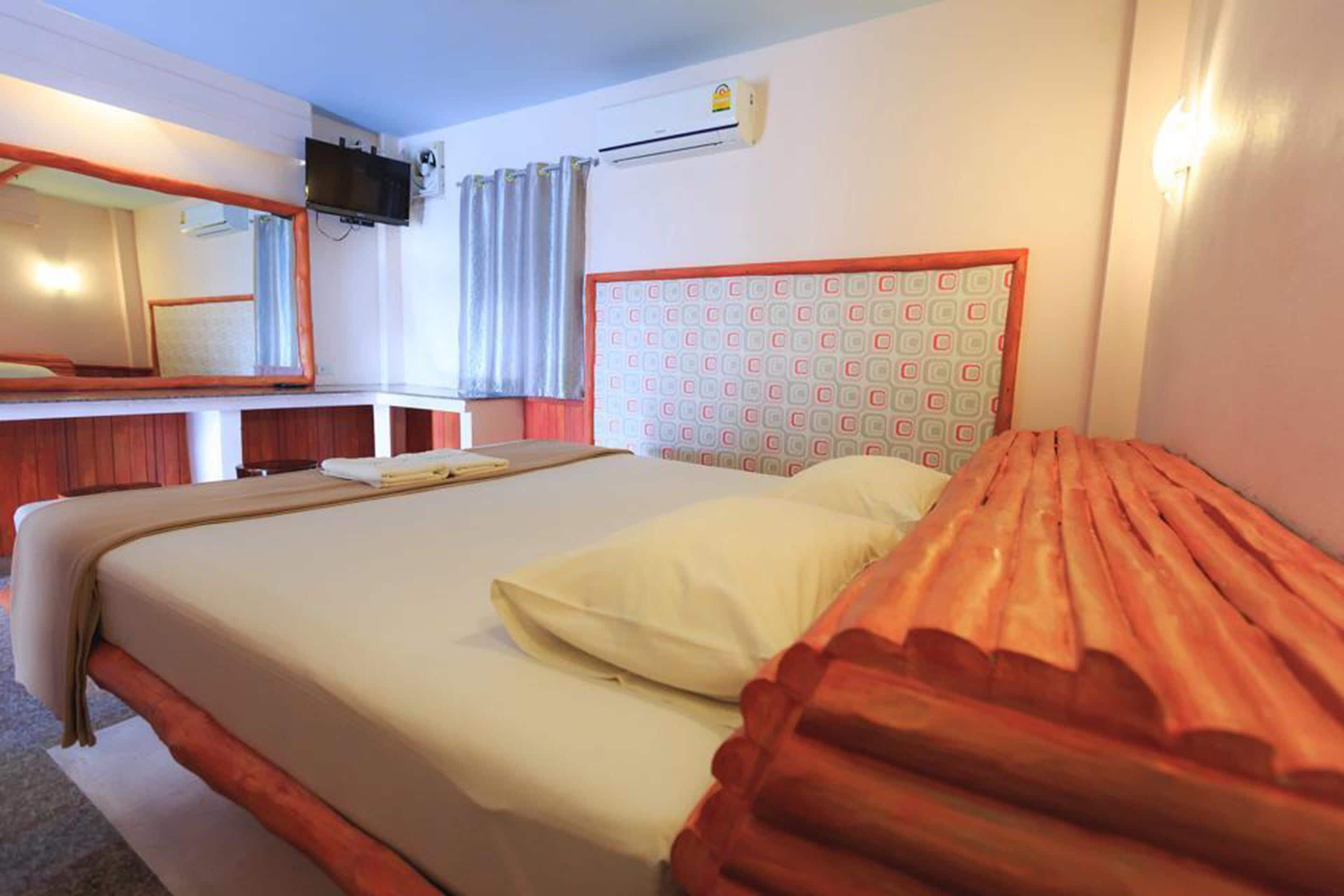 A hotel room with a bed, a TV mounted on the wall, and an air conditioning unit.