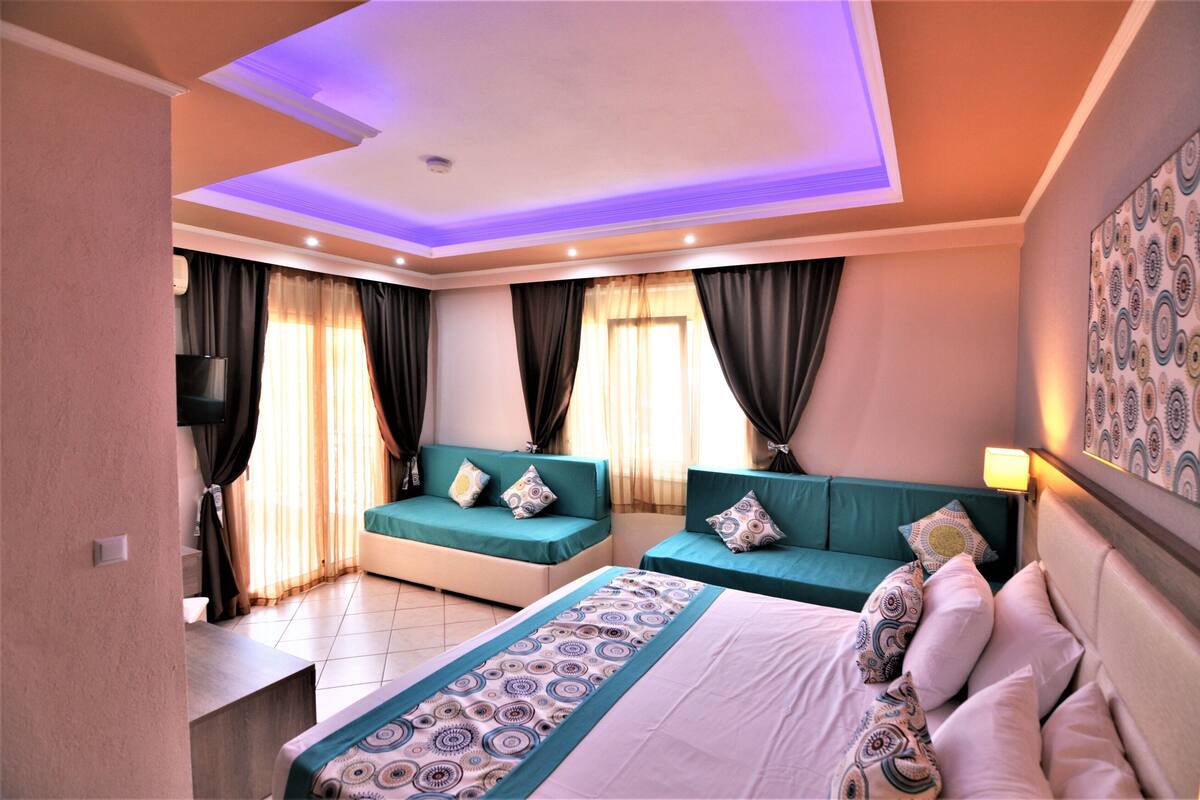 A hotel room with a bed, two sofas, a TV, and a ceiling light.
