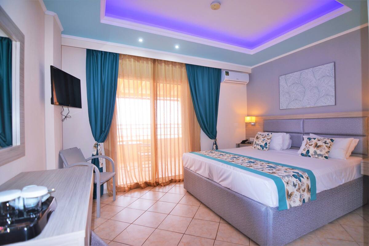 A hotel room with a bed, a desk, a TV, and a window with curtains.