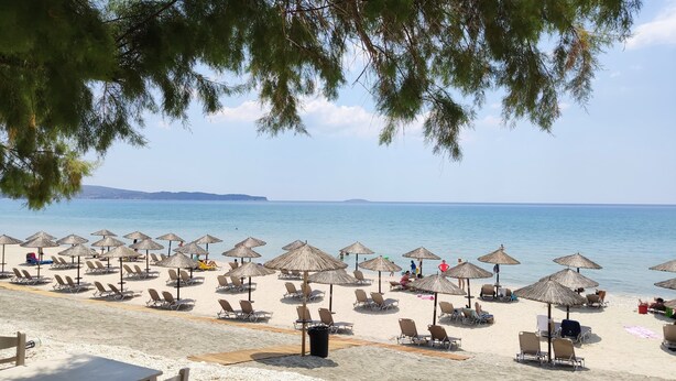 Una platja amb files de gandules i para-sols de palla, cel blau i mar tranquil·la.