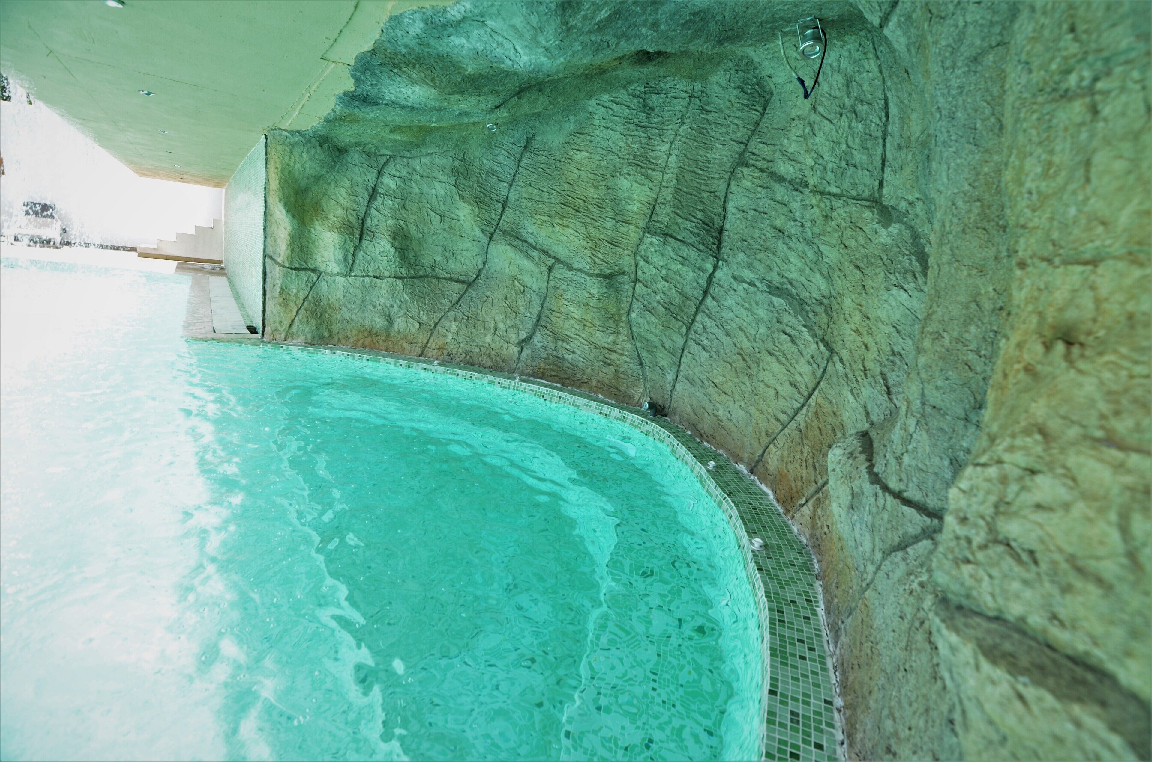 A swimming pool with clear water, surrounded by a rocky wall.