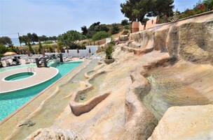 Una piscina con un diseño escalonado único, rodeada de sillones de descanso y sombrillas.