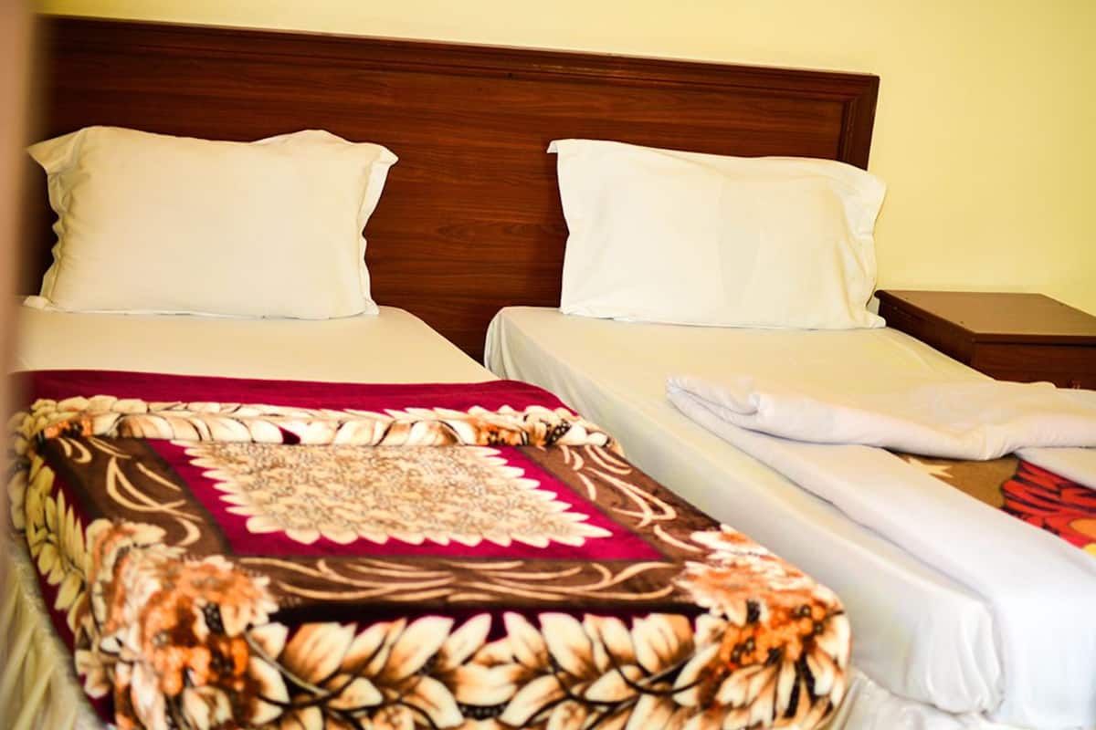 A hotel room with two beds, each with white linens and pillows, a wooden headboard, and a decorative throw blanket.