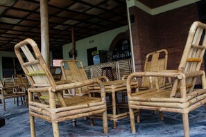 A covered outdoor seating area with bamboo chairs and a brick wall in the background.