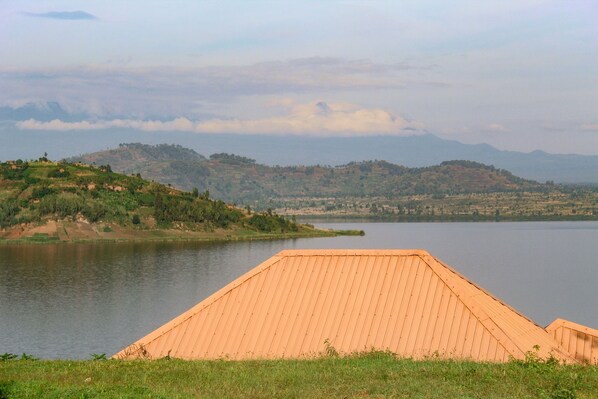A large, open wooden structure by a lake with hills in the background.