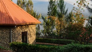 A stone building with a red roof, surrounded by lush greenery and a view of a mountain and lake.