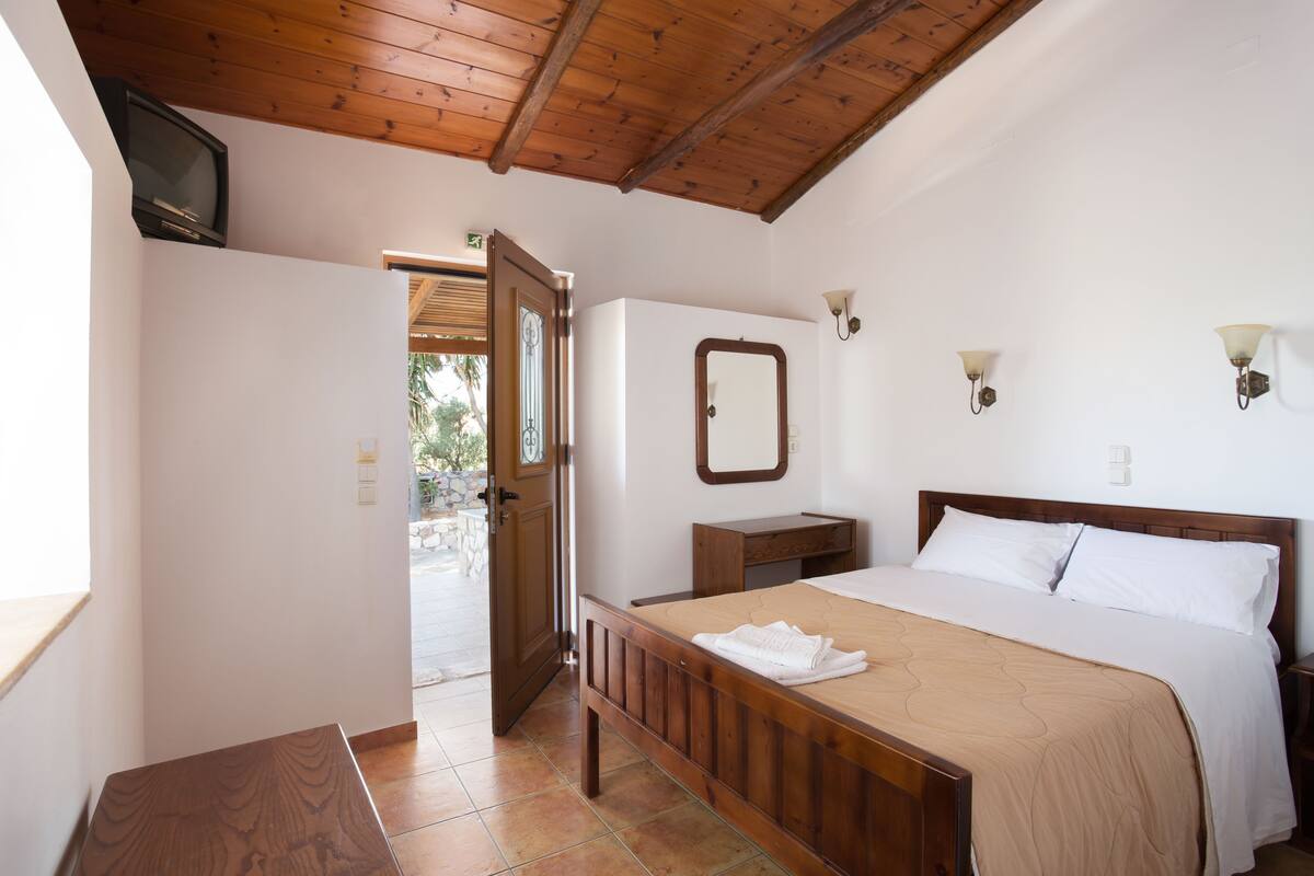 Un dormitorio con una cama de madera, una mesita de noche, un espejo y un televisor en la pared.