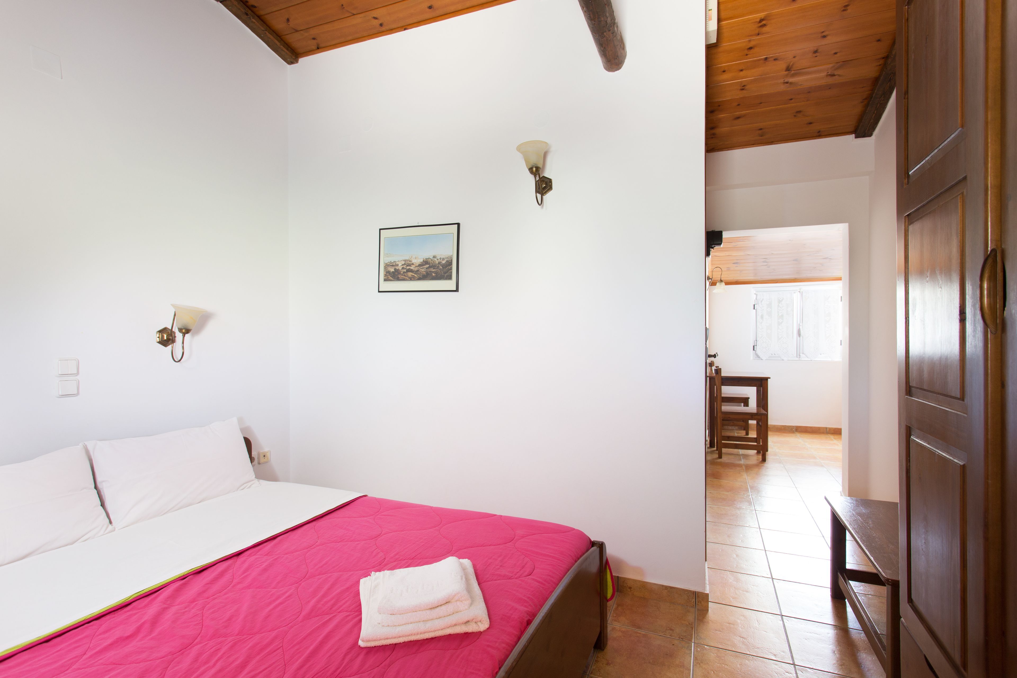 A bedroom with a bed, a wooden ceiling, a wall-mounted light, and a framed picture.