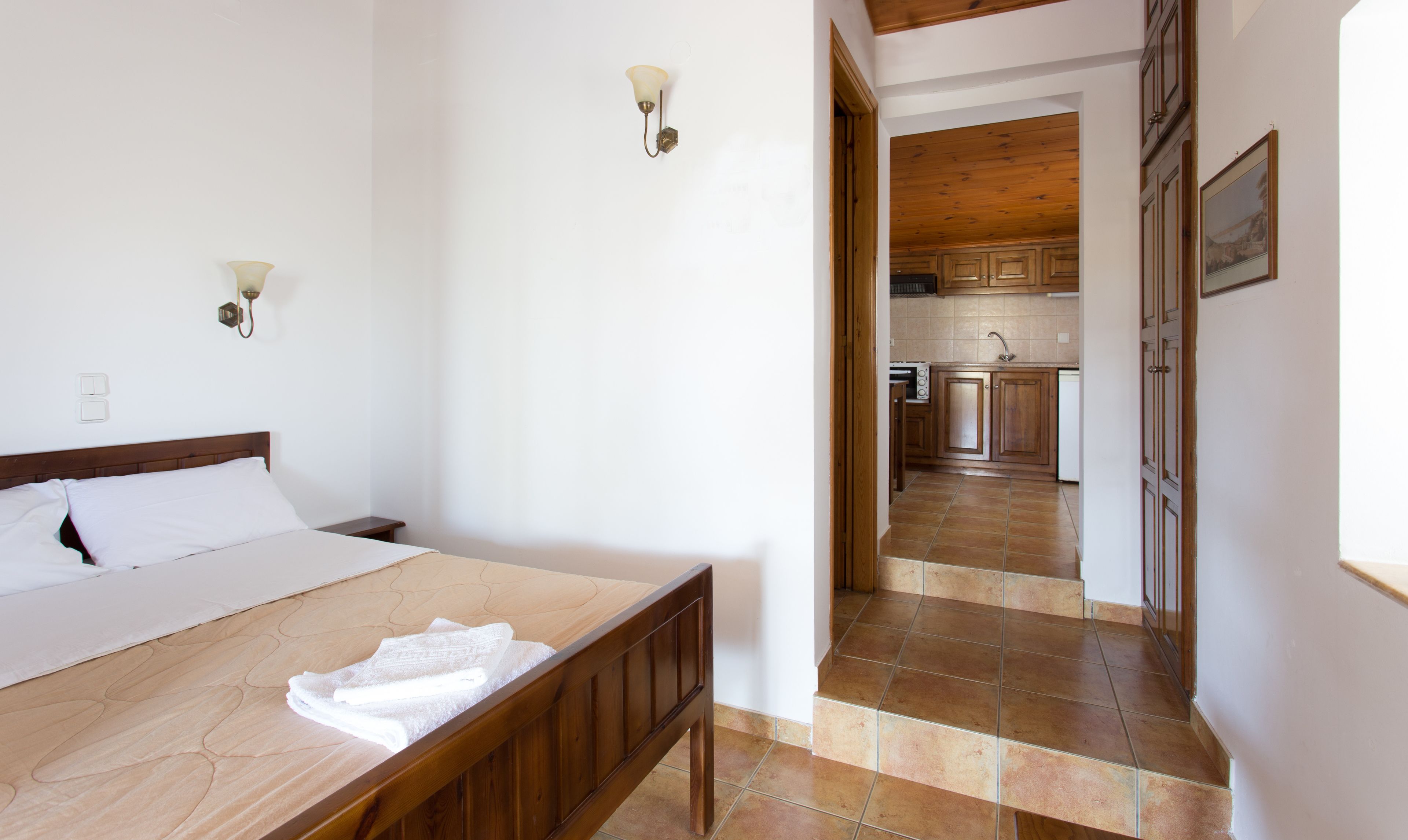 A bedroom with a wooden bed, white linens, and a bathroom with a wooden door.