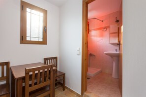 A room with a wooden dining table and chairs, a window, and a shower area with a sink.