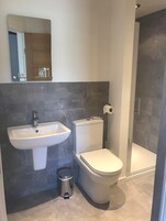 A modern bathroom with a pedestal sink, toilet, and a glass shower enclosure.