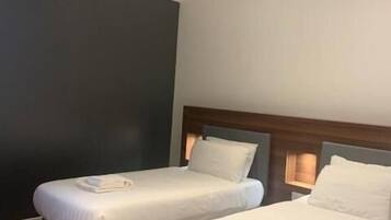 A hotel room with two single beds, a dark accent wall, and a sloped ceiling with exposed beams.