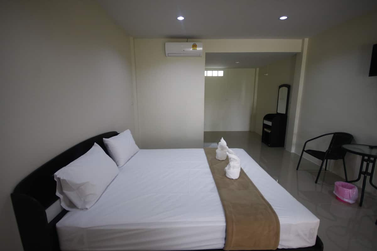 A hotel room with a bed, a bedside table, a chair, and an air conditioning unit.