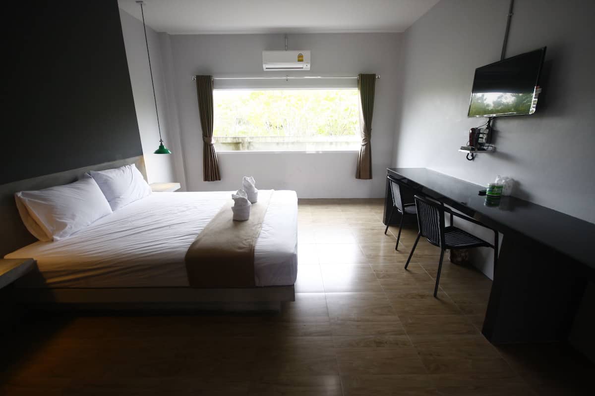 A hotel room with a bed, a desk, a chair, a TV, and a window with curtains.