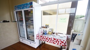 A room with a refrigerator stocked with beverages, a table with food items, and a water dispenser.
