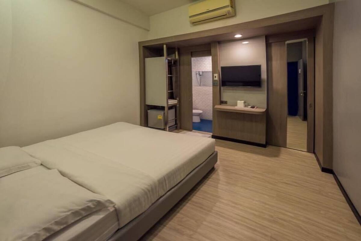 Une chambre d’hôtel comprenant un lit, un téléviseur fixé au mur, une salle de bain avec douche et toilettes, ainsi qu’un petit bureau avec un miroir.