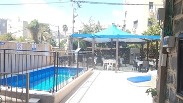 A swimming pool with a blue tarp-covered area, a fenced patio, and outdoor seating.