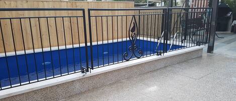 Una piscina con un borde de baldosas y valla de madera.