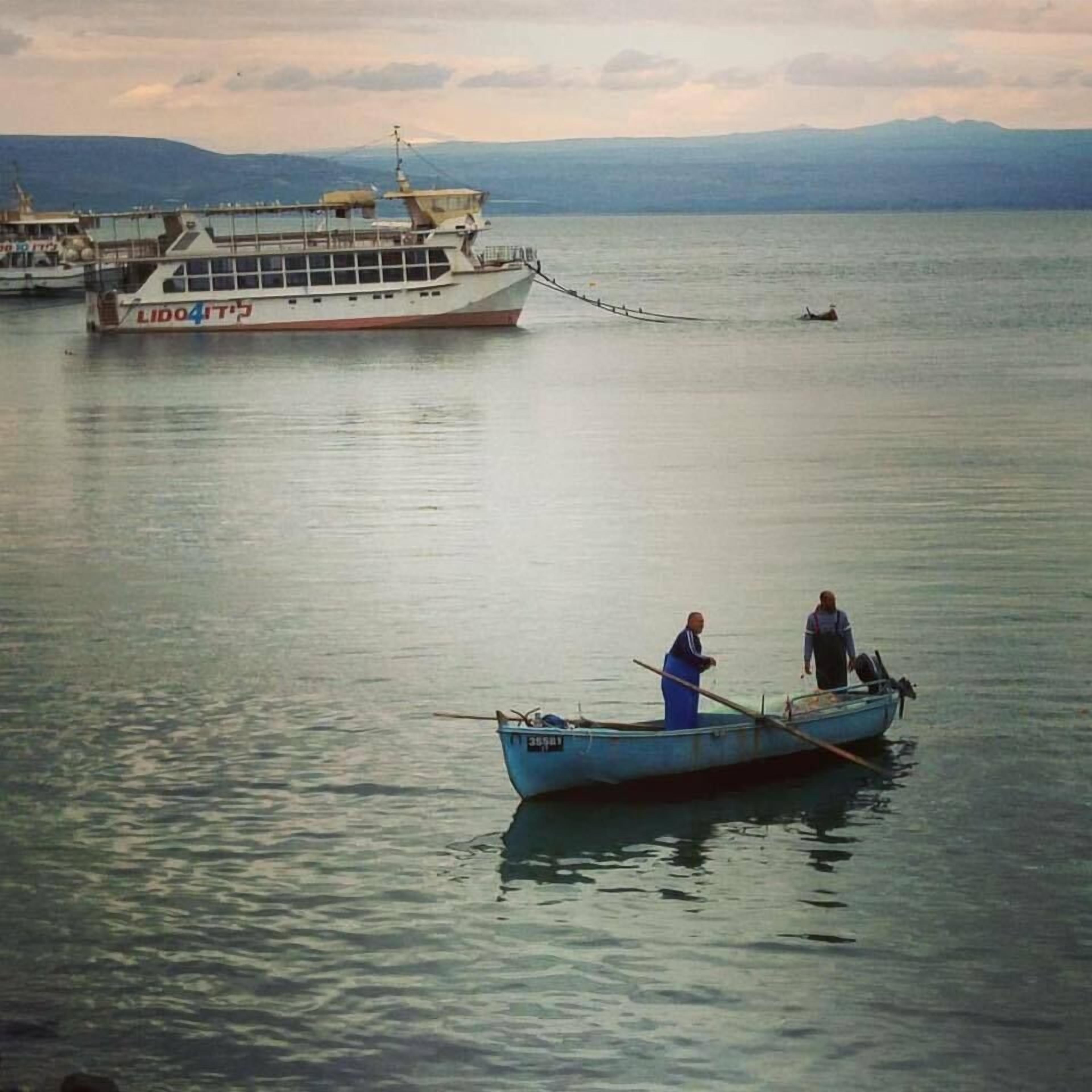 A calm lake with a large ferry and a small boat with two people.