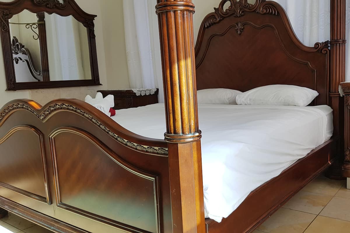 Un lit à baldaquin avec une finition en bois, une table de chevet avec des tiroirs et un miroir au mur.