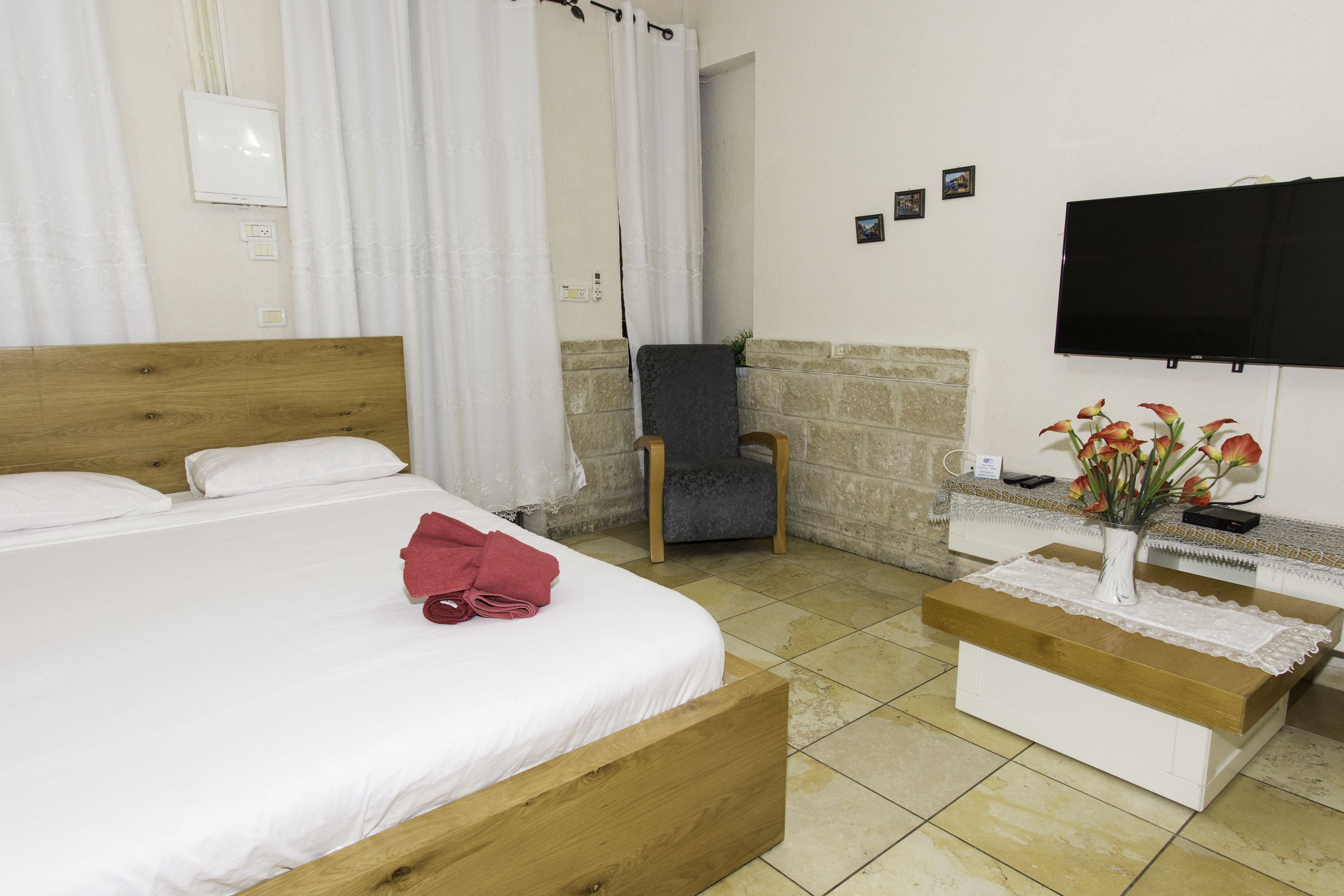 A hotel room with a bed, a chair, a TV, and a small table with a vase of flowers.