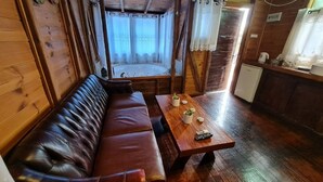A wooden cabin interior with a leather sofa, a wooden table with a remote control, and a small refrigerator. - Lake Mansion (Tiberias)