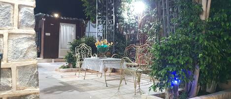 Un patio al aire libre con una mesa y sillas, rodeado de muros de piedra y follaje.