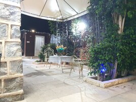 Un patio al aire libre con una mesa y sillas, rodeado de muros de piedra y follaje.