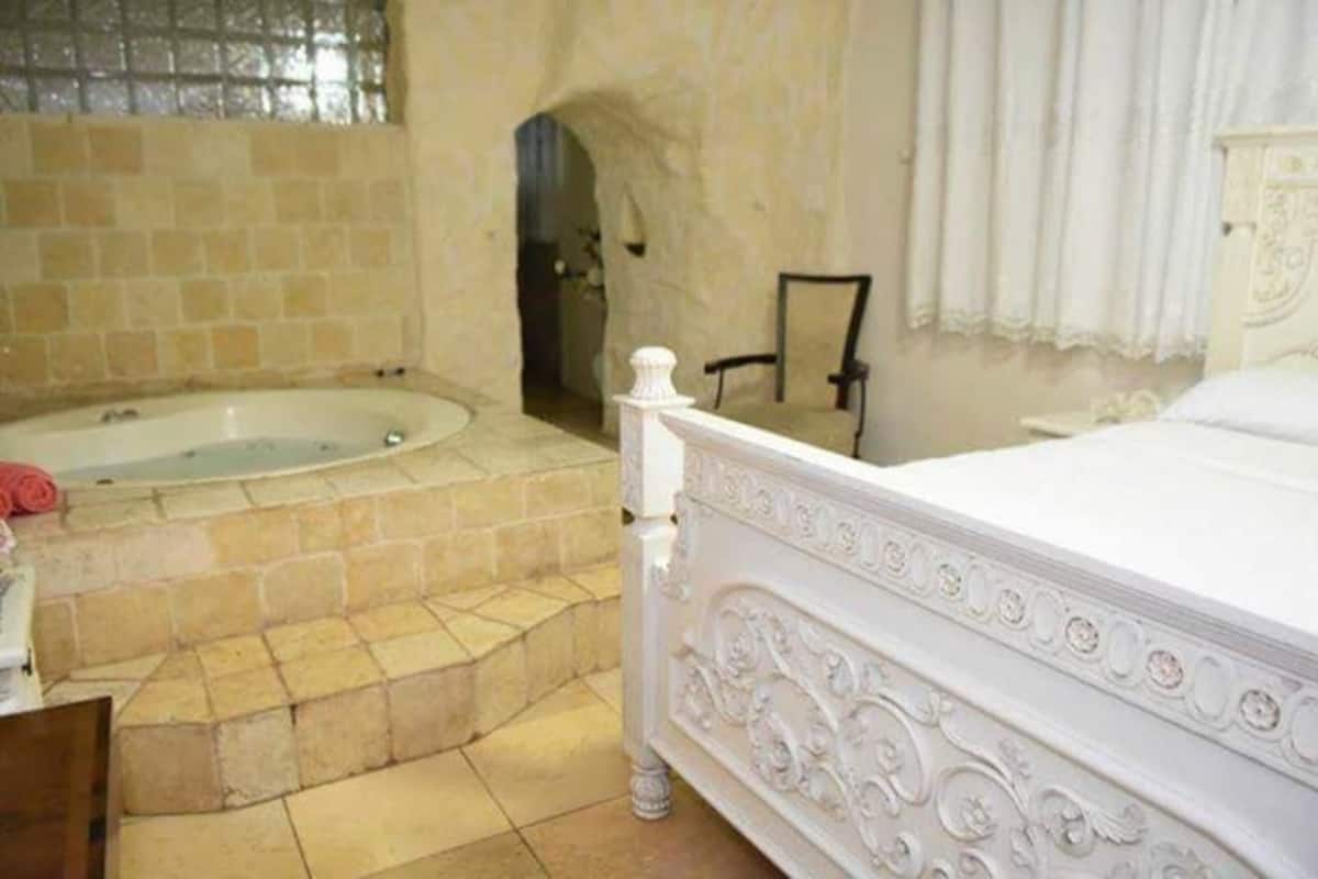 Une chambre dotée d’une grande baignoire, d’un lit blanc à baldaquin et d’un sol carrelé en pierre.
