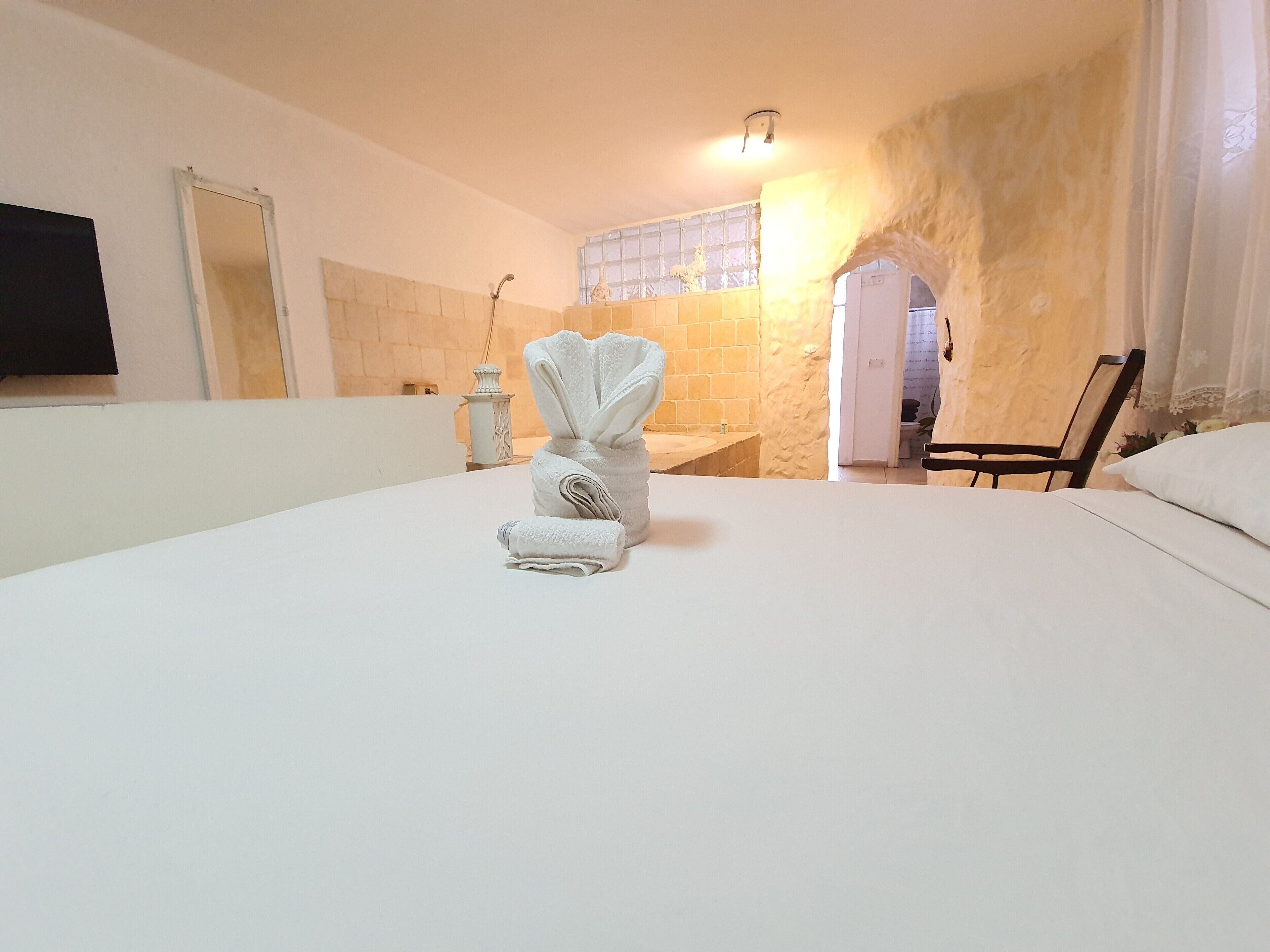 Une chambre d’hôtel avec un grand lit, une salle de bain avec un mur en pierre, un miroir et une chaise.