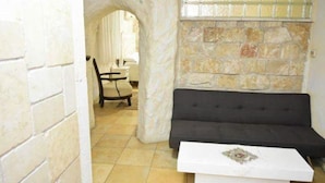 A room with a stone wall, a black sofa, and a white table. - Lake Mansion (Tiberias)