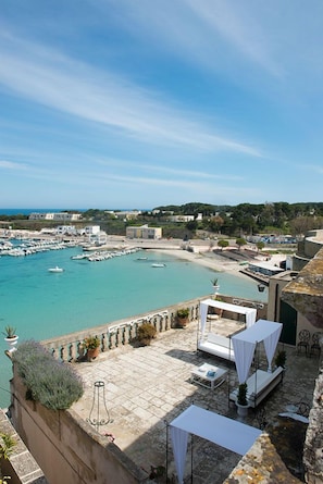 A coastal terrace with outdoor seating, a view of the marina, and buildings in the background. - B&B Centro Storico (Otranto)