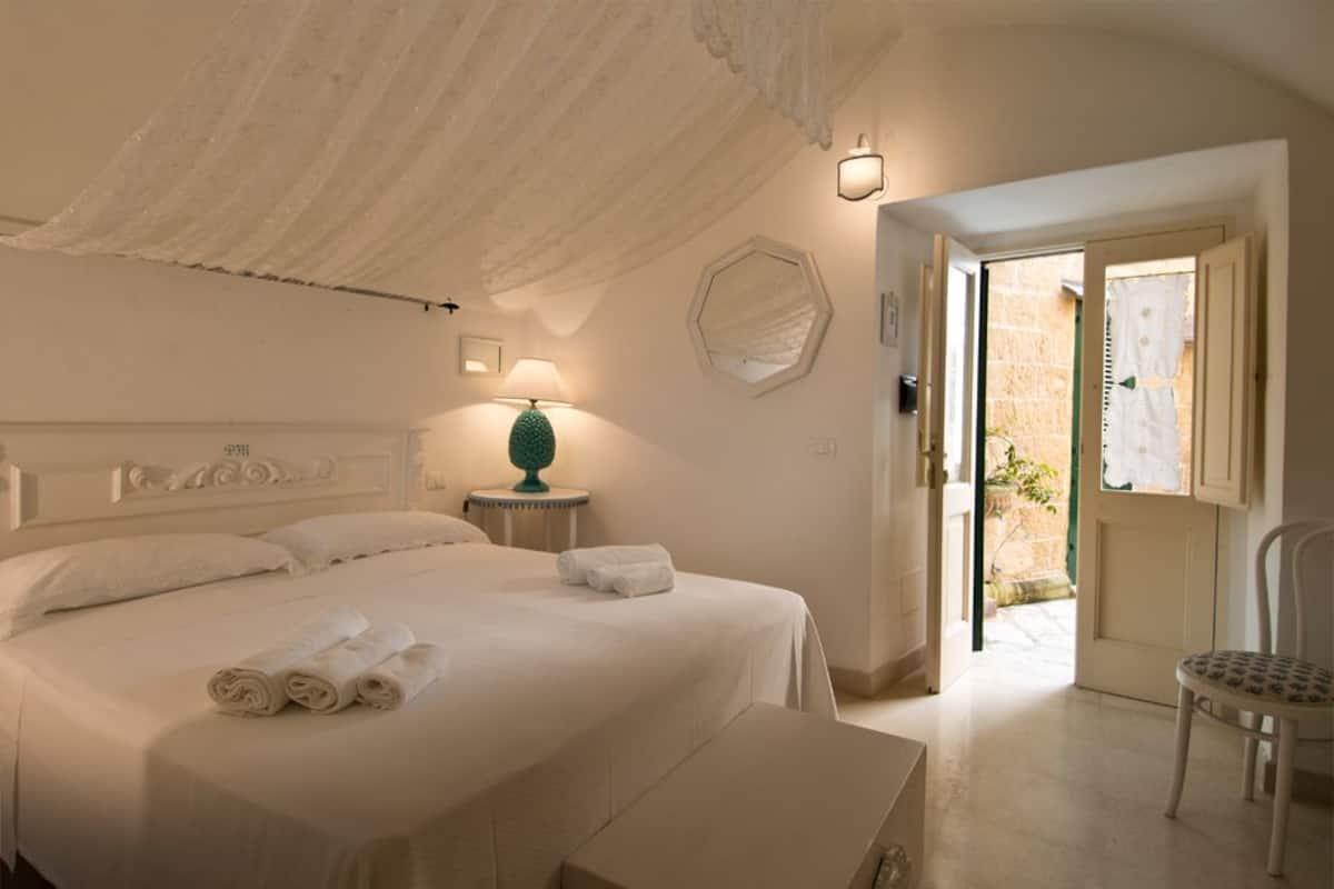 Un dormitorio con cama, lámpara de noche y una silla.
