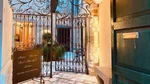 An arched entrance with a wrought iron gate, a signboard, and a stone pathway leading to a courtyard with plants and a seating area. - B&B Centro Storico (Otranto)