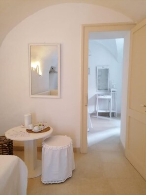 A narrow hallway with a white door leading to a bathroom. A small table with a white cloth and a basket is visible in the foreground. - B&B Centro Storico (Otranto)
