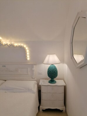 A bedroom with a bed, a nightstand with a lamp, a mirror, and a string of lights on the wall. - B&B Centro Storico (Otranto)