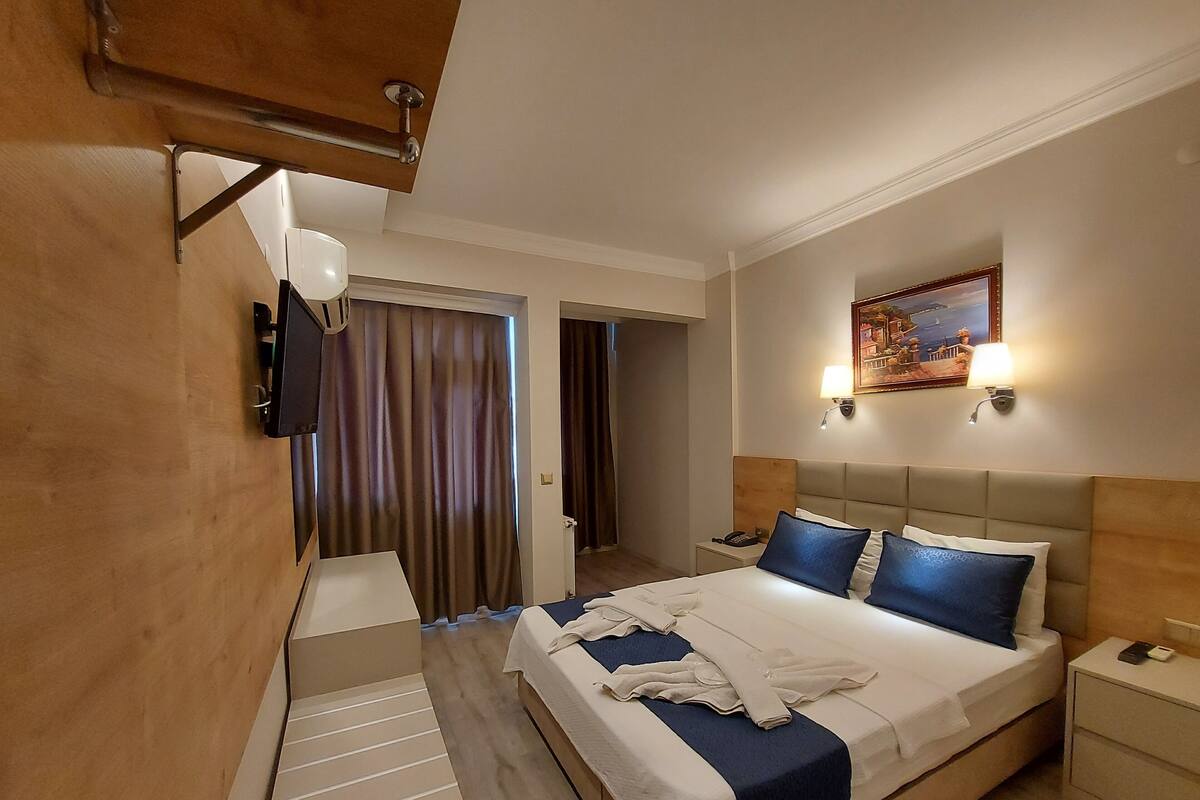 A hotel room with a bed, bedside tables, a lamp, a painting on the wall, and a door leading to another room.