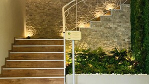 Un escalier en bois avec une rampe métallique, un mur en pierre et un mur végétal.