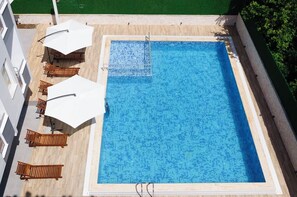 A rooftop swimming pool with wooden loungers and white umbrellas, surrounded by a wooden deck and a green lawn. - Afsin Hotel (Konyaalti)