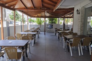 An outdoor cafe with multiple tables and chairs, a television screen, and a tiled floor. - Afsin Hotel (Konyaalti)