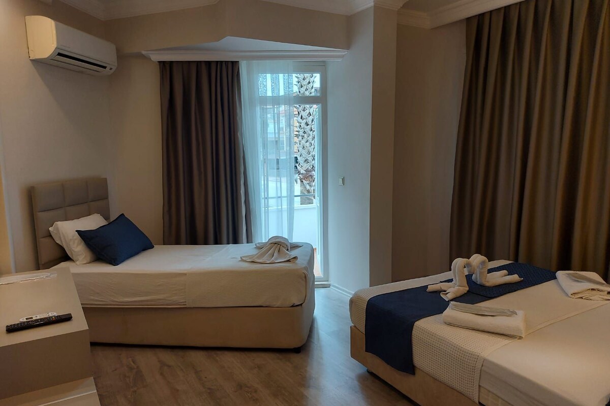 A hotel room with two beds, a desk, and an air conditioning unit.