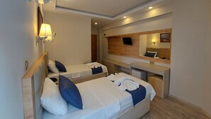 Une chambre d’hôtel avec deux lits, un bureau, un miroir et un téléviseur fixé au mur.