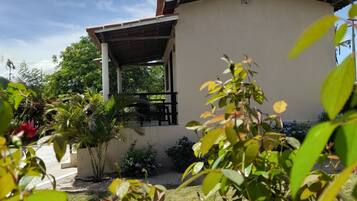 A building with a flat roof, a covered porch, and a garden with various plants and flowers.